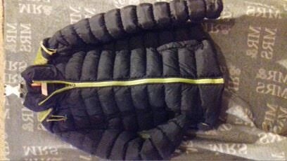 Czarna, pikowana kurtka z żółtym zamkiem błyskawicznym leżąca na wzorzystym, szarym tle.