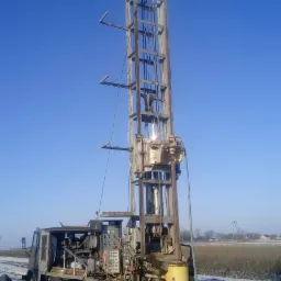 Mobilna wiertnica do studni głębinowych w trakcie pracy na zasnieżonym polu, widoczny numer rejestracyjny pojazdu.