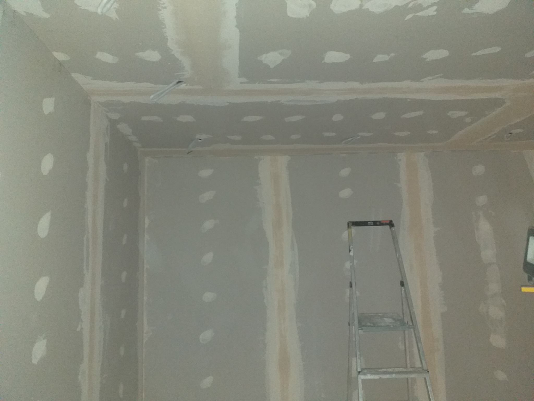 Wnętrze w trakcie prac wykończeniowych: ściany i sufit pokryte płytami, widoczne łączenia i miejsca po wkrętach wymagające szpachlowania, drabina oparta o ścianę, przygotowane do dalszych etapów prac.