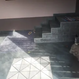 Wykończone wnętrze z szarymi płytkami podłogowymi, schodami wyłożonymi kamieniem dekoracyjnym, fioletowym dywanem i jasnym dywanikiem z geometrycznym wzorem, widok z góry w jasnym świetle.