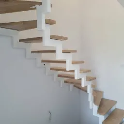 Nowoczesne schody wspornikowe z drewnianymi stopniami i białymi wspornikami, widok z dołu, surowy stan wykończenia ścian.