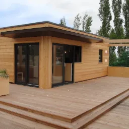 Nowoczesna, drewniana altana z tarasem i oświetleniem. Drewniana elewacja, przesuwne drzwi, donica z rośliną. Tło: drzewa. Detal: punktowe oświetlenie tarasu.