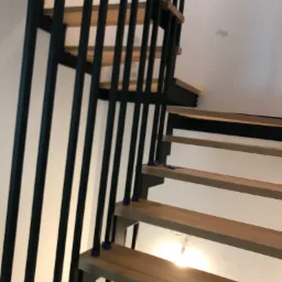 Drewniane schody z czarną metalową balustradą, widok z dołu, niebieskie podkładki pod słupkami balustrady.