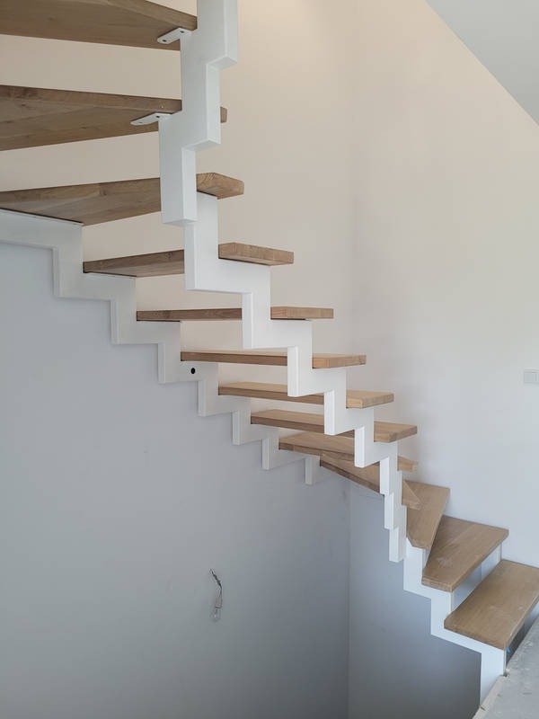 Nowoczesne schody wspornikowe z drewnianymi stopniami i białymi wspornikami, widok z dołu, surowy stan wykończenia ścian.