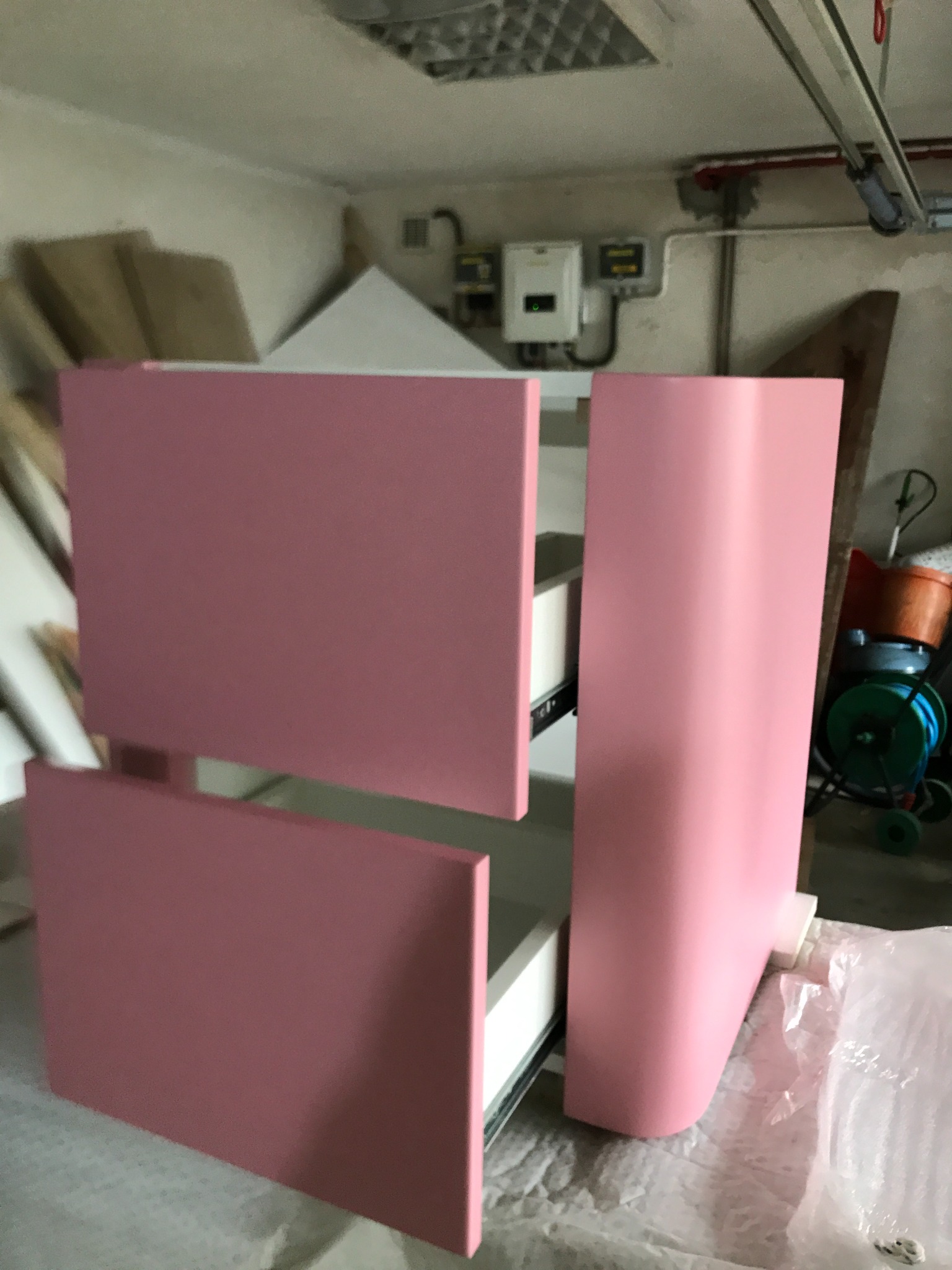 Różowa szafka z szufladami w trakcie montażu, widoczne prowadnice, tło warsztatowe z narzędziami i materiałami. Ujęcie z bliska, w pomieszczeniu.