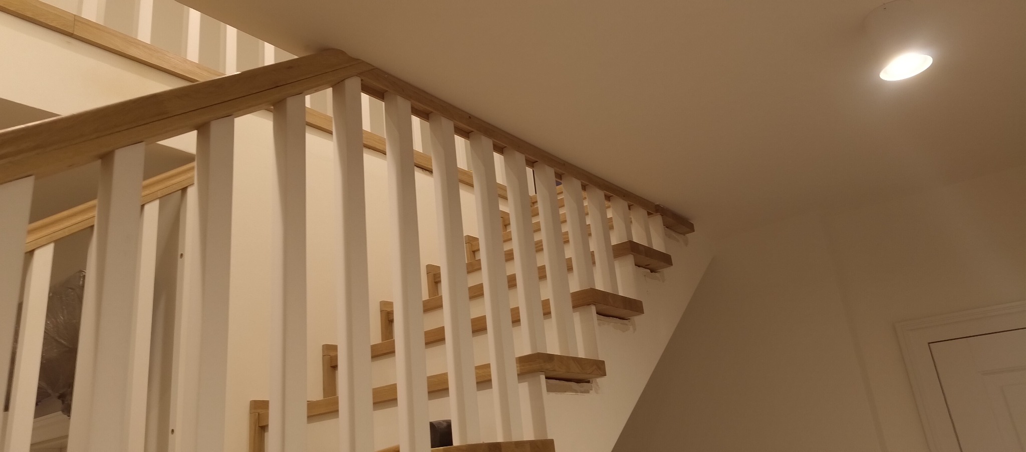 Fragment drewnianych schodów z białymi balustradami. Ujęcie z dołu, widoczne stopnie i poręcz. Świeże malowanie, jasne wnętrze.