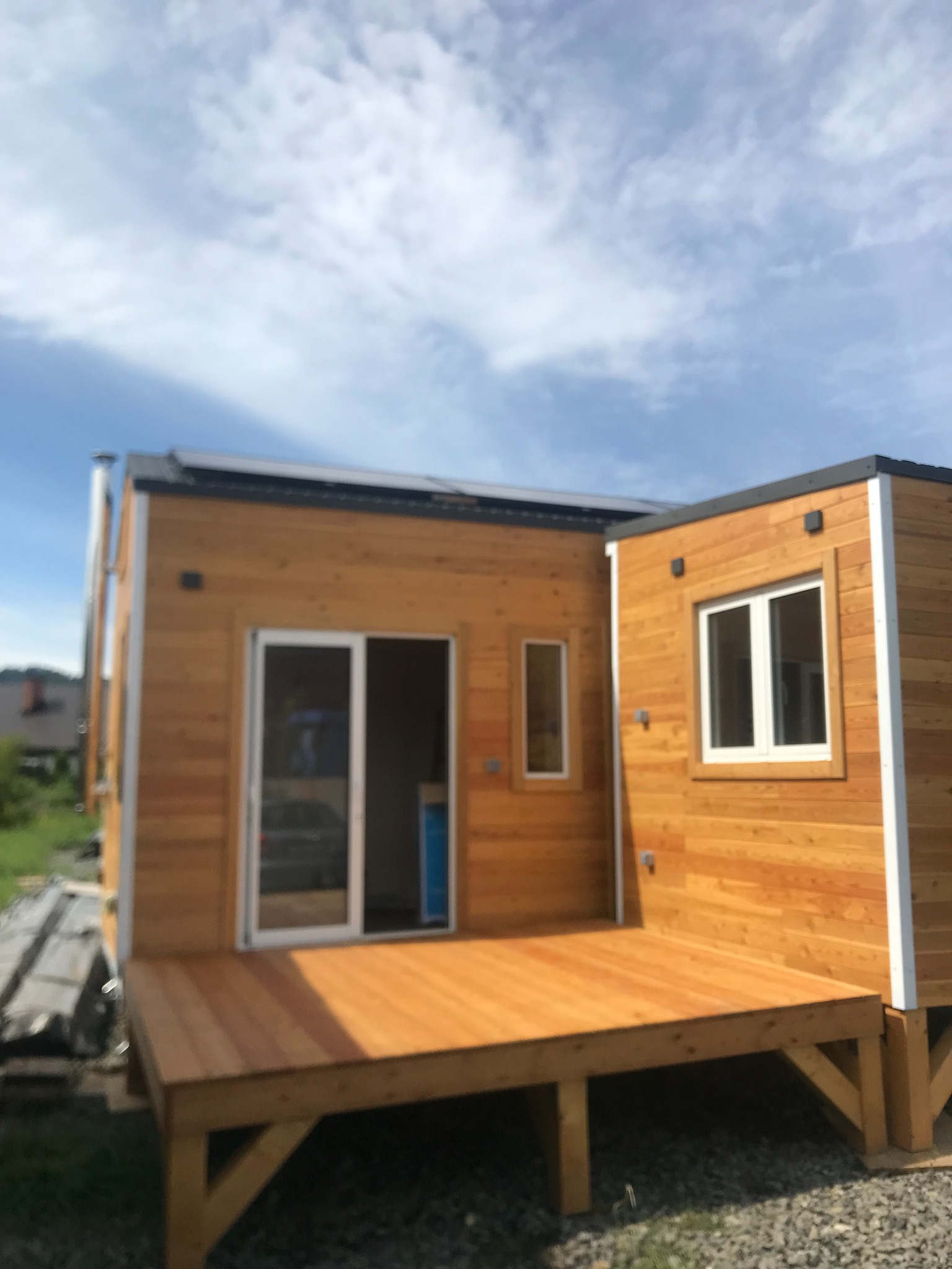 Nowoczesny, drewniany dom modułowy z tarasem, wykończony jasnym drewnem, z widocznymi oknami i drzwiami przesuwnymi, na tle błękitnego nieba.