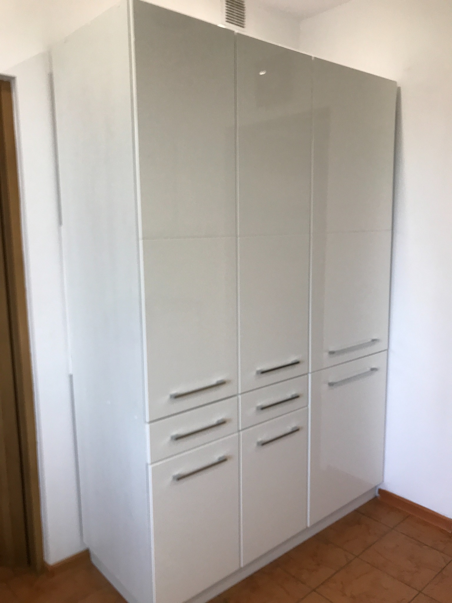 Biała szafa wnękowa z połyskiem i metalowymi uchwytami, wykonana na wymiar w Krzywaczce. Minimalistyczny design, gładkie fronty.