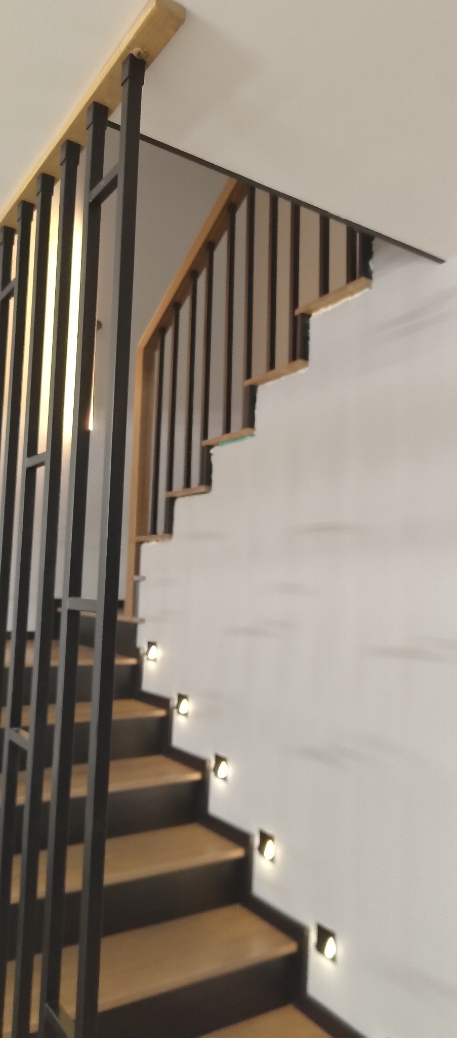 Nowoczesne schody drewniane z czarnymi balustradami i subtelnym oświetleniem punktowym wzdłuż stopni. Minimalistyczny design, jasne drewno, ciemne akcenty.