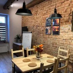 Jasne drewniane krzesła i stół z podkładkami, dekoracja z jesiennych liści w szklanym wazonie na tle ściany z czerwonej cegły w pokoju z oknem.