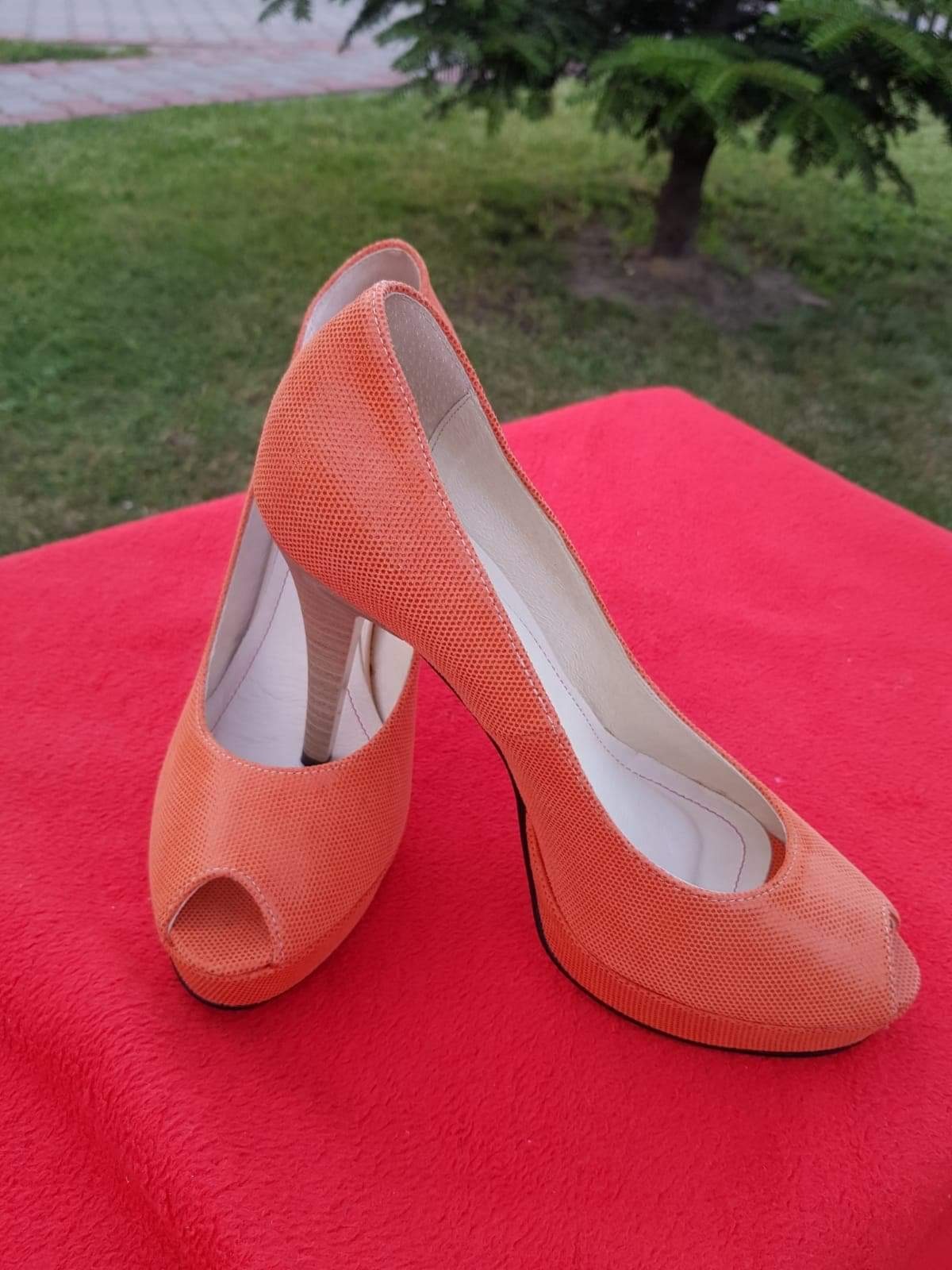 Pomarańczowe szpilki z odkrytymi palcami na czerwonym tle, z fakturą przypominającą skórę węża i drewnianymi obcasami.