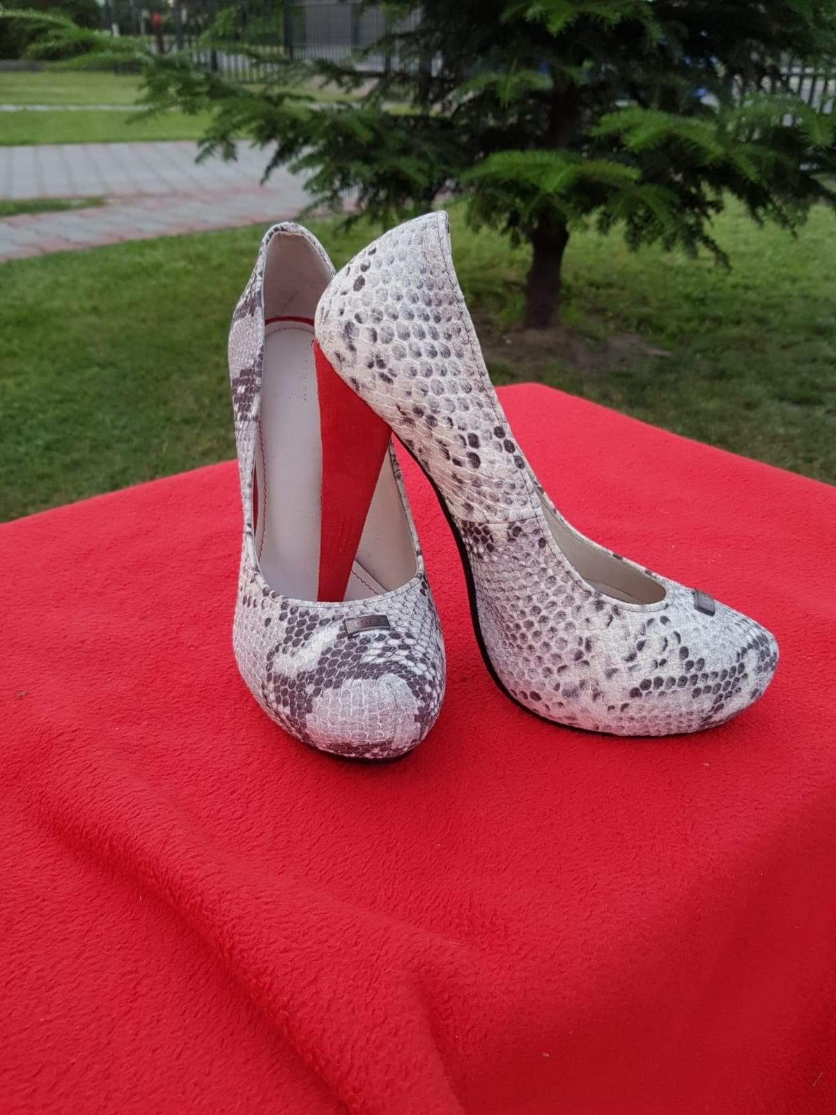 Para damskich czółenek na wysokim obcasie, z wzorem imitującym skórę węża, ustawiona na czerwonym materiale na tle zieleni.