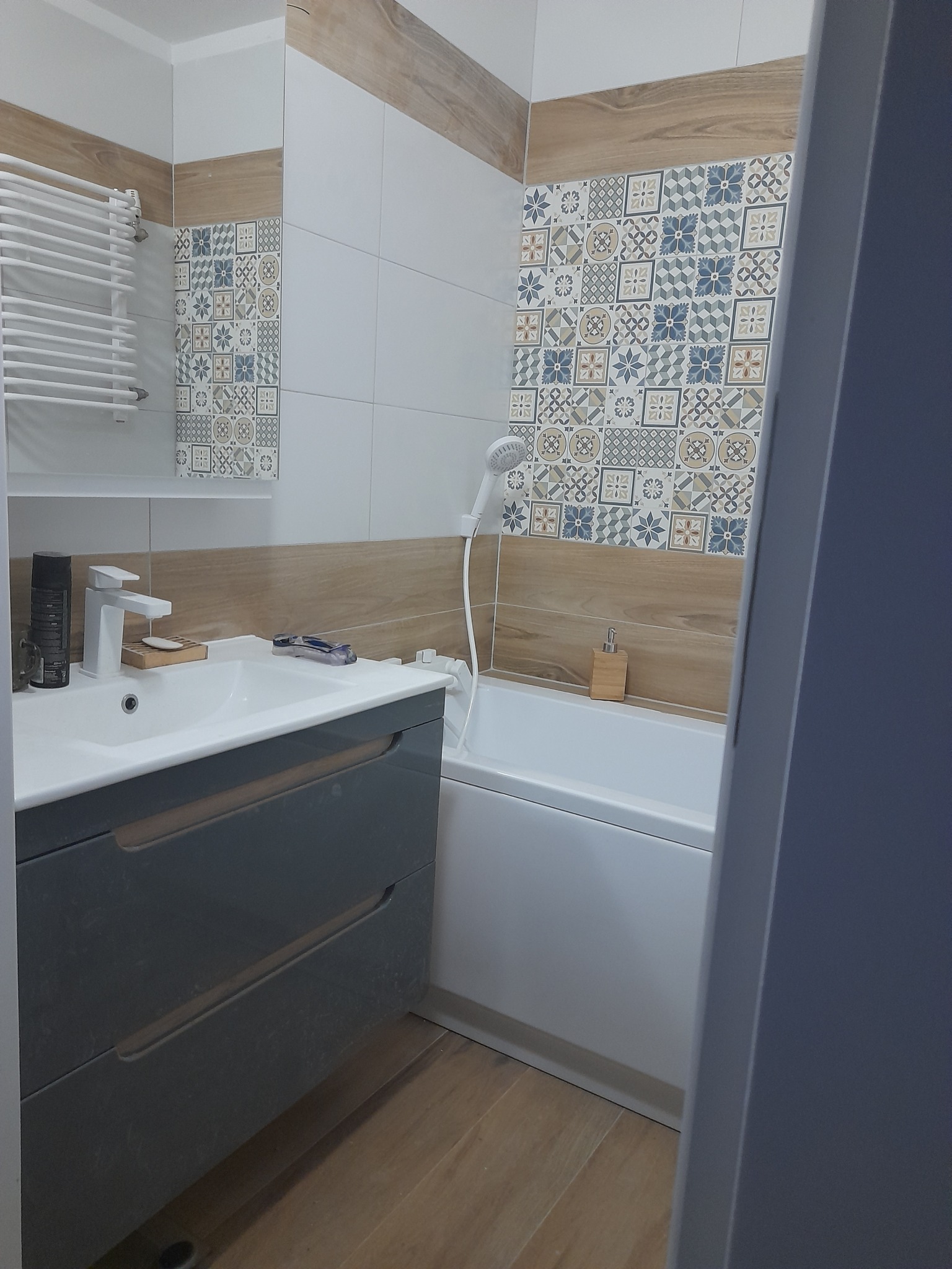 Wykończona łazienka z szarą szafką pod umywalką, białą wanną i płytkami dekoracyjnymi na ścianie.