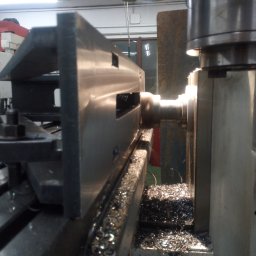 Adeko System Janusz Dźwigoń - Metalowy element obrabiany na tokarce, widoczne wióry i oświetlenie punktowe.