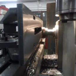 Metalowy element obrabiany na tokarce, widoczne wióry i oświetlenie punktowe.