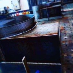 Adeko System Janusz Dźwigoń - Metalowe elementy konstrukcyjne, w tym perforowany pierścień i prostopadłościenne kształtowniki, ułożone na perforowanym stole spawalniczym w warsztacie.