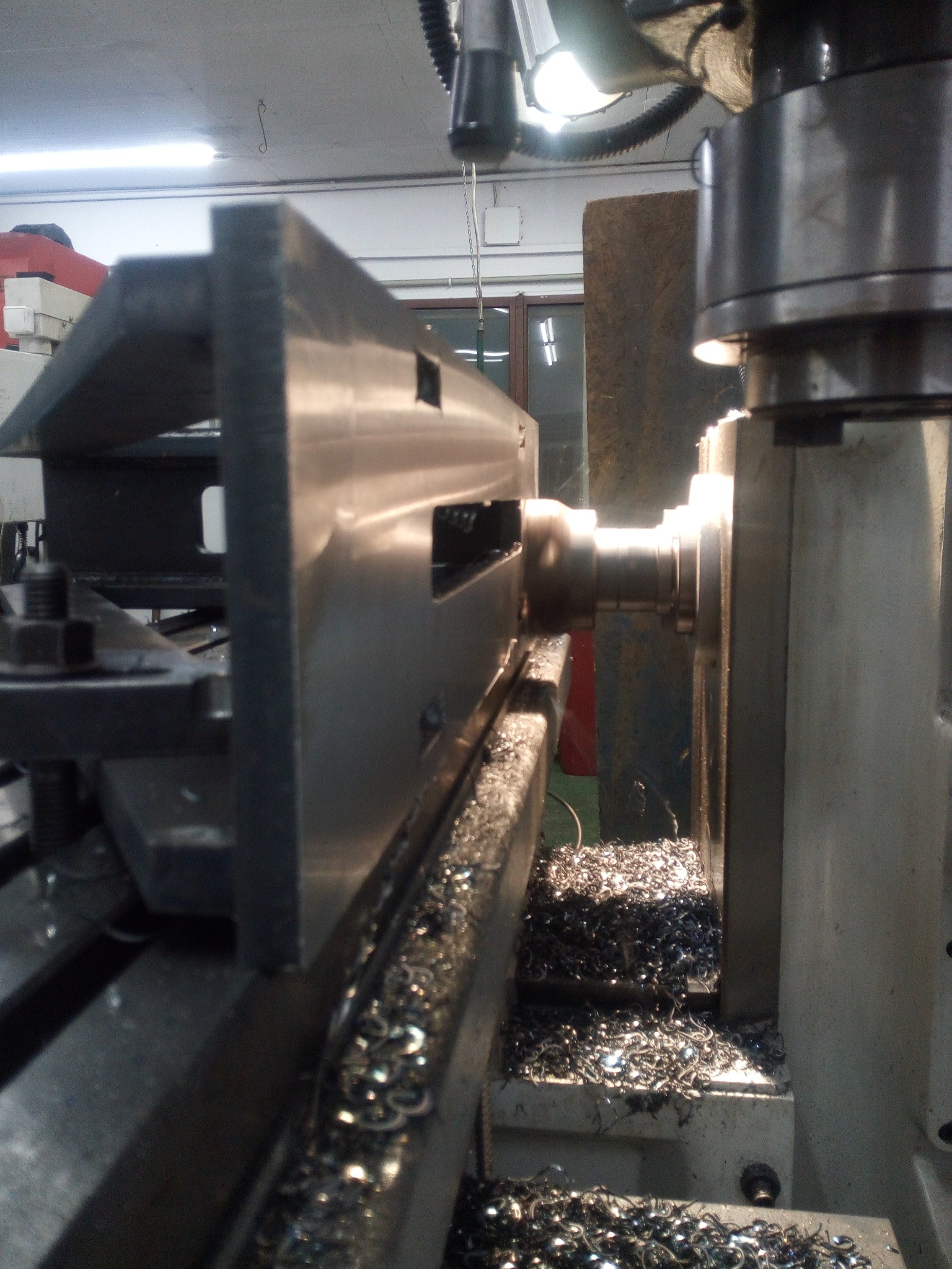 Metalowy element obrabiany na tokarce, widoczne wióry i oświetlenie punktowe.