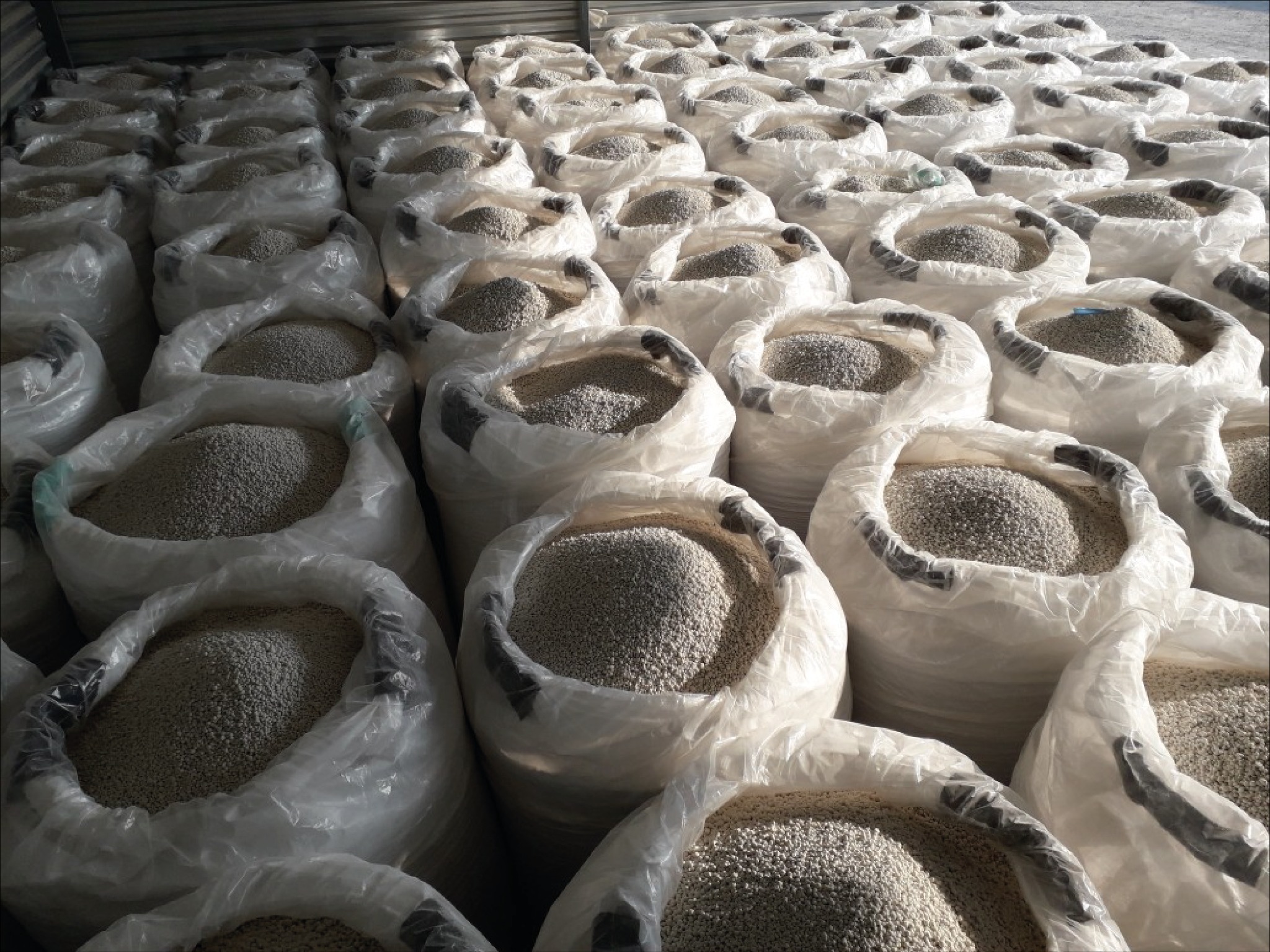Rzędy worków z granulowanym materiałem, prawdopodobnie nawozem, wypełnionych po brzegi i gotowych do transportu lub magazynowania, oświetlonych z góry.