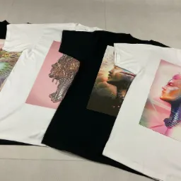 Rząd ułożonych koszulek z nadrukami przedstawiającymi abstrakcyjne portrety kobiece, w tym grafiki z elementami zwierzęcymi i pikselowymi efektami.