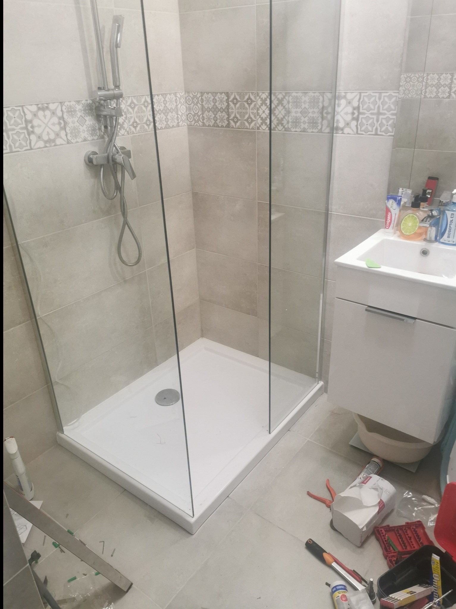 Montaż kabiny prysznicowej z brodzikiem w łazience w Warszawie, widoczne narzędzia i materiały budowlane na podłodze, płytki ceramiczne na ścianach z dekoracyjnym pasem.