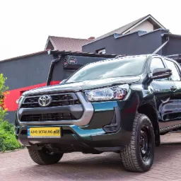 Zielony Toyota Hilux po detailingu, zaparkowany na kostce brukowej przed budynkiem z logo ADHD Detailing na ścianie.