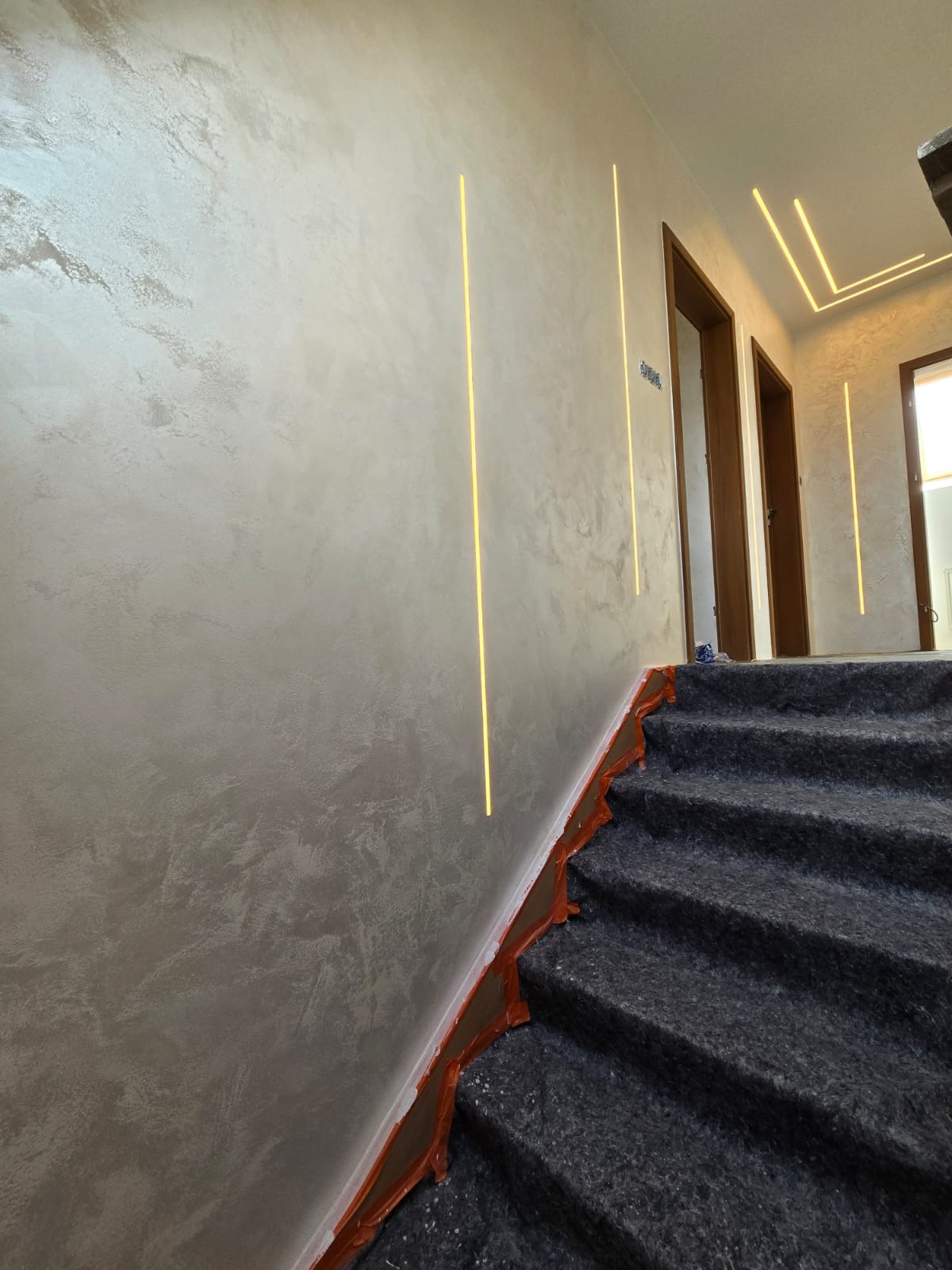 Elegancka ściana ze strukturą i pionowymi liniami LED na klatce schodowej, zabezpieczone schody, ciepłe światło, wykończenie wnętrz w nowoczesnym stylu.