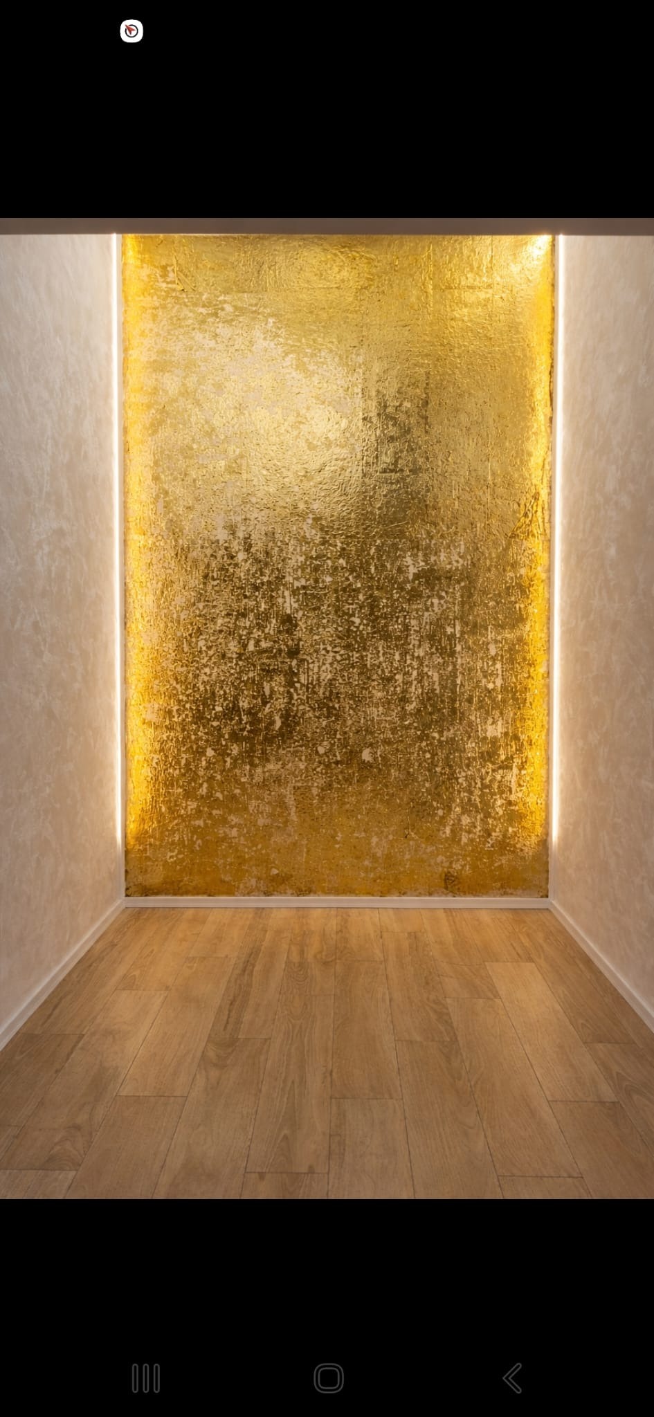 Pokój z drewnianą podłogą i ścianą pokrytą złotą, teksturowaną farbą, oświetloną pionowymi pasami LED po bokach. Nowoczesny design.