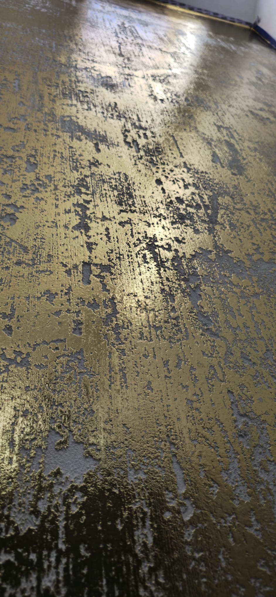 Dekoracyjna ściana z efektem złota i szarości, wykonana techniką strukturalną. Widoczne nieregularne wzory i faktura, tworzące unikalny, artystyczny wygląd.