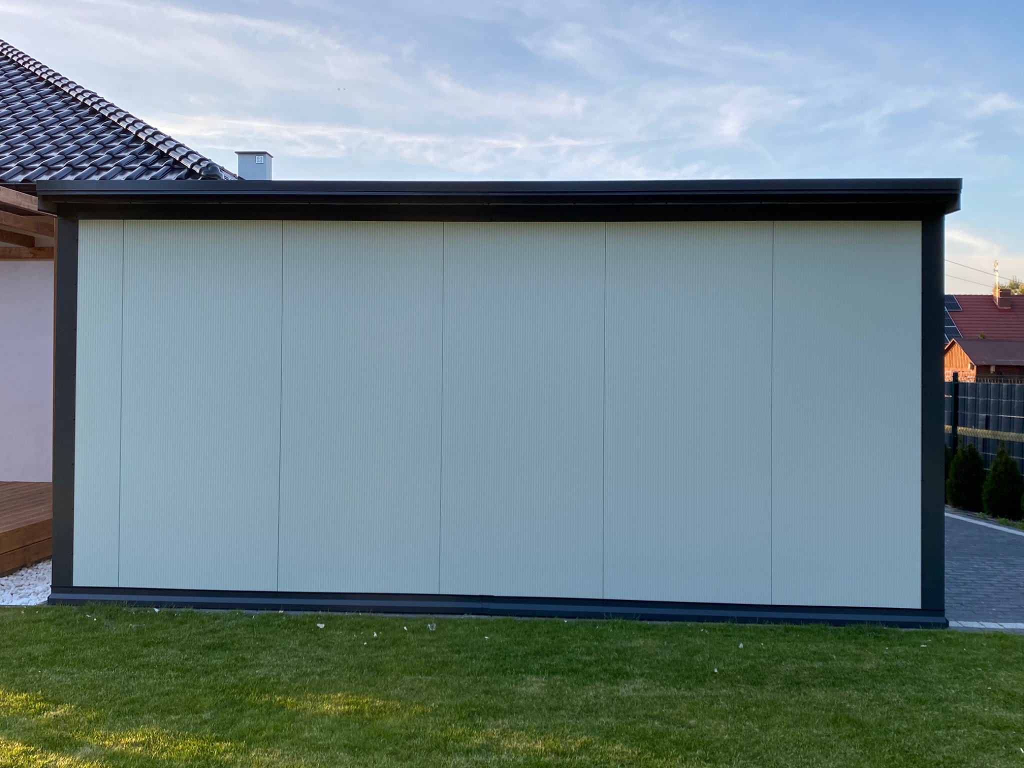 Gotowa ściana hali z płyt warstwowych w jasnym odcieniu, widoczna z zewnątrz, z fragmentem dachu i trawnikiem w kadrze.