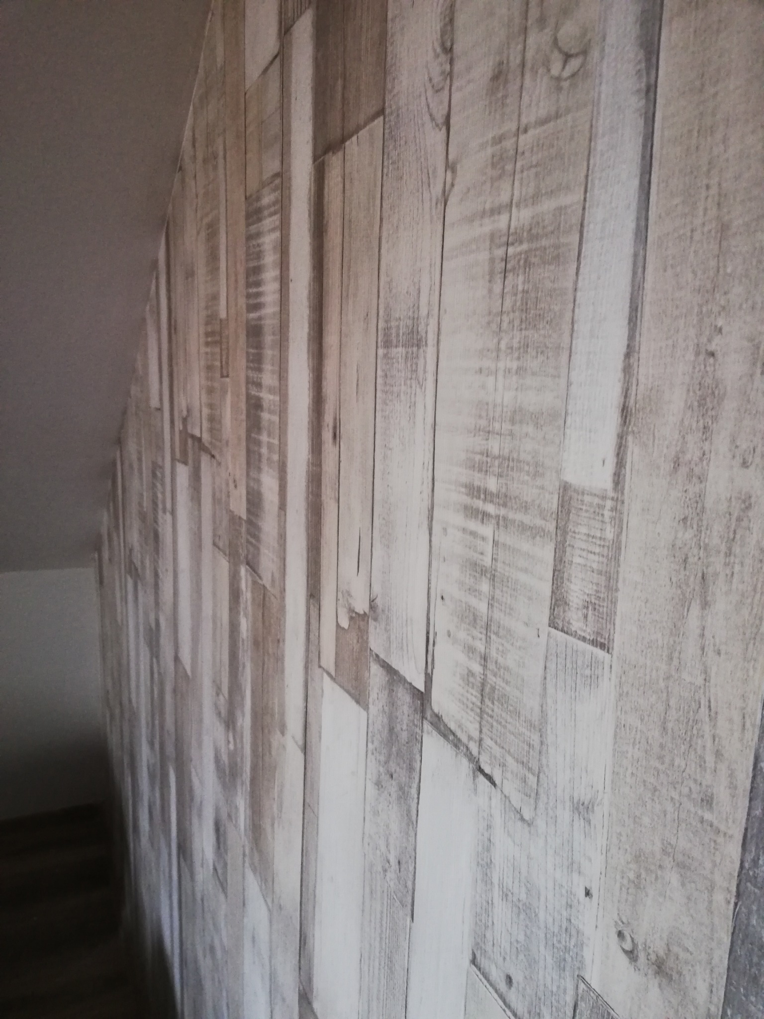 Ściana w pokoju na poddaszu wykończona panelami ściennymi imitującymi stare, bielone drewno, ułożonymi pionowo.