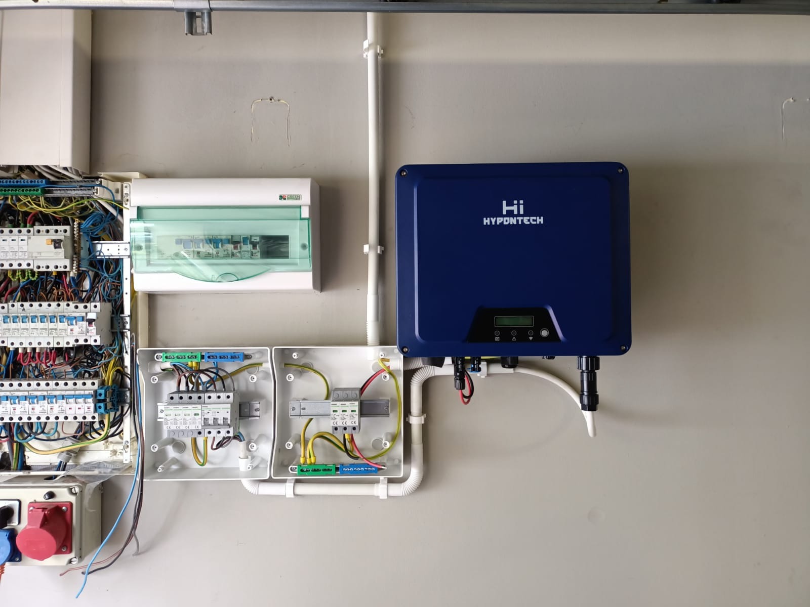 Niebieski inwerter Hypdotech zamontowany na ścianie obok rozdzielnic elektrycznych z okablowaniem w rurkach PCV.