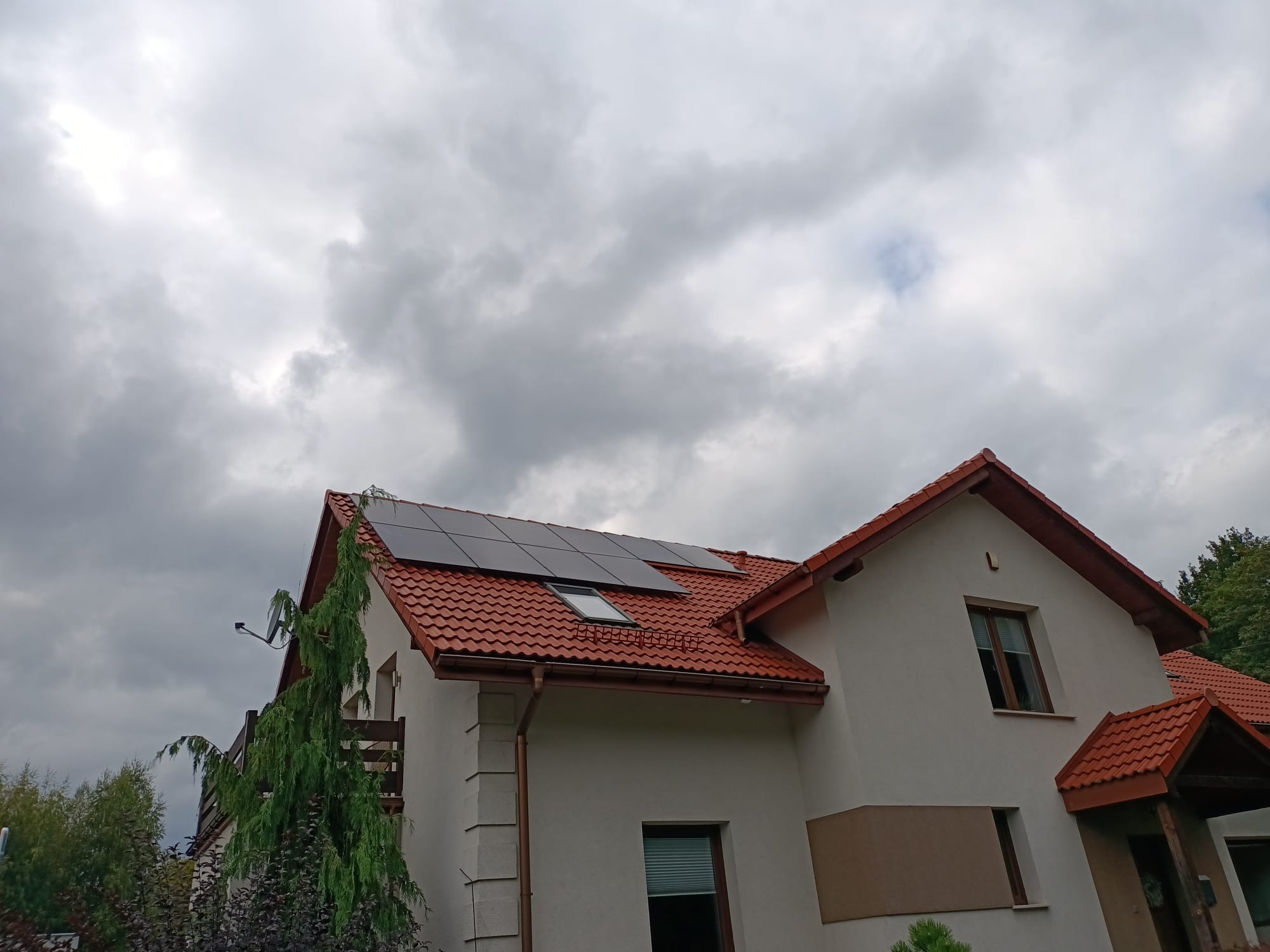 Panele fotowoltaiczne zamontowane na dachu domu jednorodzinnego w Bielsku-Białej, widoczne z poziomu gruntu na tle pochmurnego nieba.