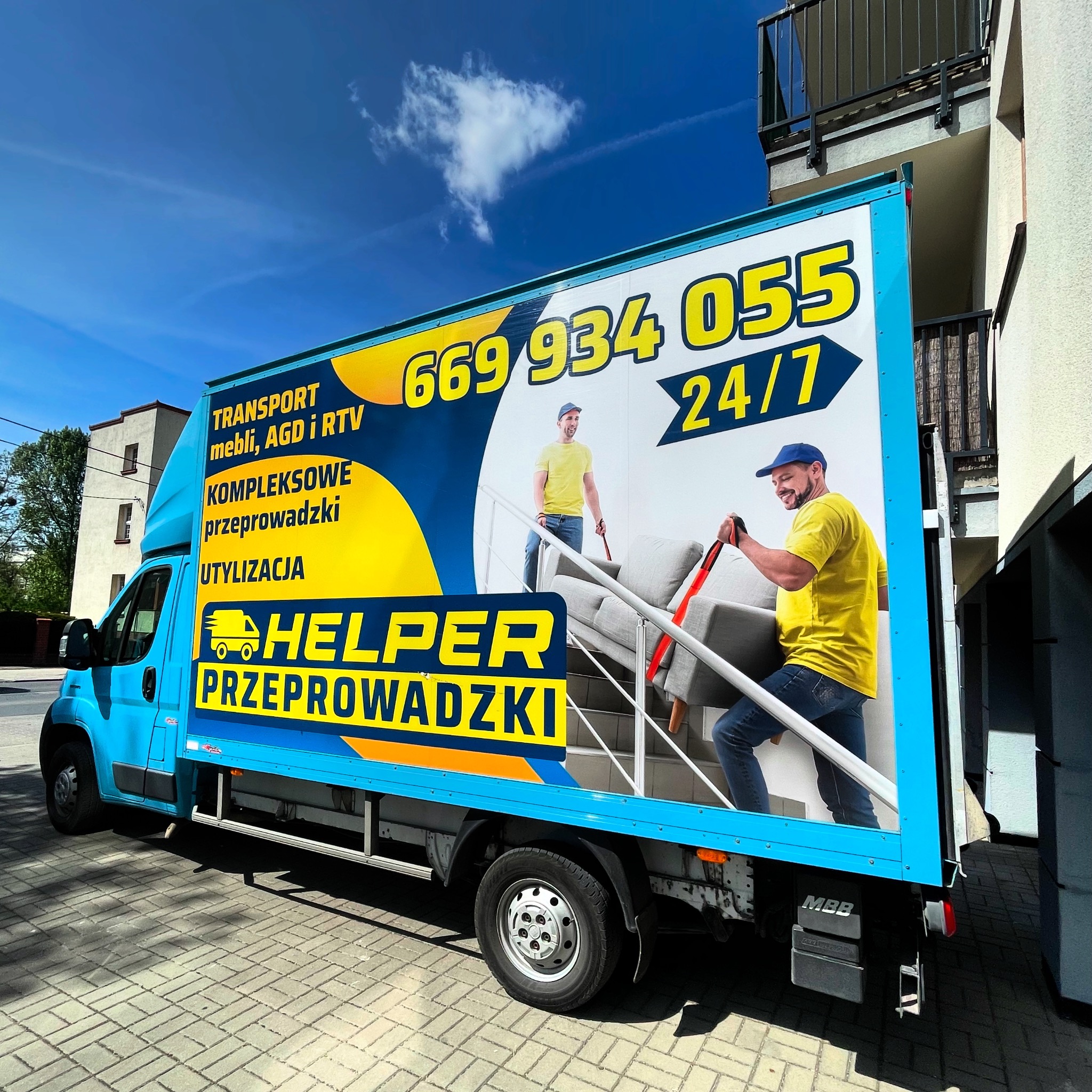 Błękitny bus z reklamą firmy przeprowadzkowej 'Helper Przeprowadzki', z numerem telefonu i hasłem 'Transport mebli, AGD i RTV'.