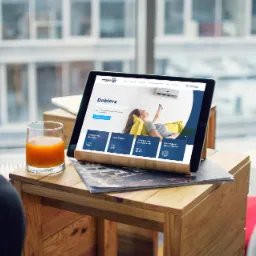 Tablet prezentuje responsywną stronę internetową firmy z branży klimatyzacji na drewnianym stoliku obok szklanki soku pomarańczowego, widok z perspektywy osoby siedzącej.