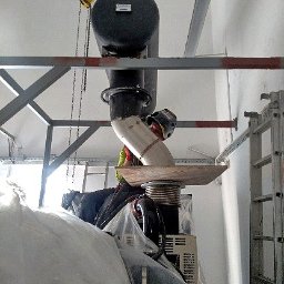 P.H.U. Welding Brothers - Montaż instalacji przemysłowej: spawacz w kasku łączy rury spawalnicze podwieszone na łańcuchu, widoczna metalowa konstrukcja wsporcza i drabina, elementy instalacji zabezpieczone folią.