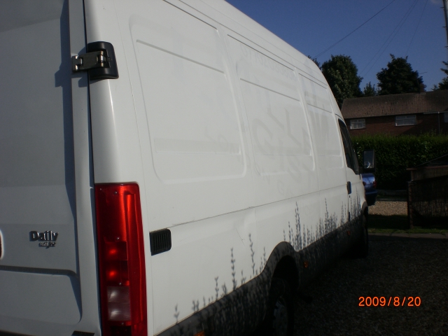 Biały samochód dostawczy Iveco Daily z 2004 roku, widok z boku, zarys roślin na dolnej części karoserii, zaparkowany na żwirowym podjeździe przed domem.