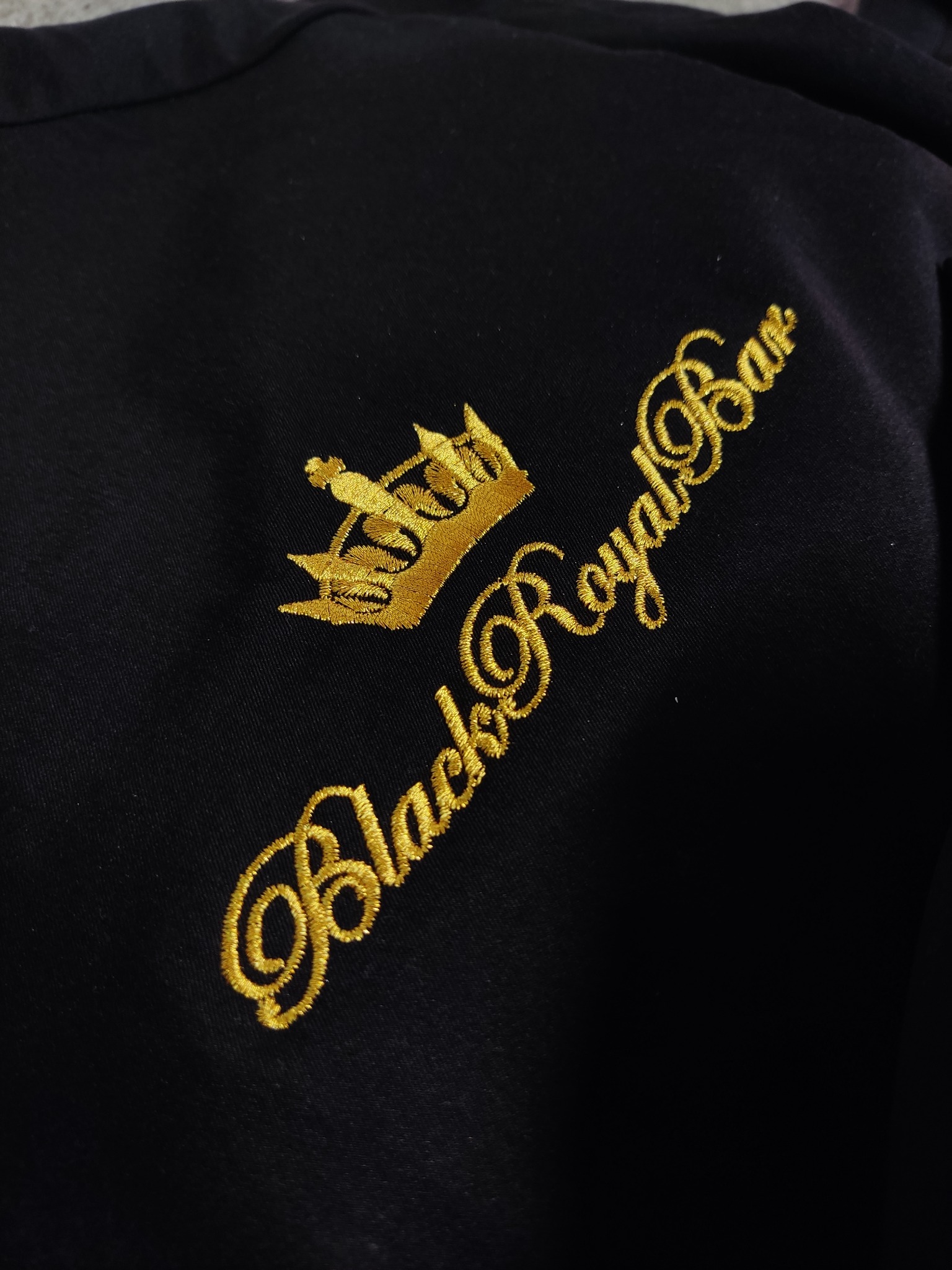 Czarna koszulka z wyhaftowanym złotą nicią logo 'Black Royal Bar' i koroną.