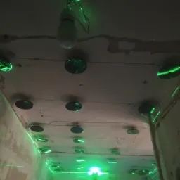 Przygotowanie do montażu sufitu podwieszanego z użyciem poziomicy laserowej, widoczne okrągłe uchwyty i linie lasera na ścianach i suficie w surowym wnętrzu.