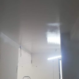 MaraBud - Świeżo pomalowane na biało wnętrze biura z widoczną drabiną i oświetleniem roboczym, przygotowane do dalszych prac wykończeniowych.