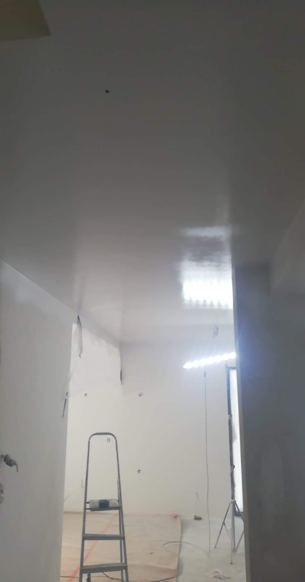 Świeżo pomalowane na biało wnętrze biura z widoczną drabiną i oświetleniem roboczym, przygotowane do dalszych prac wykończeniowych.