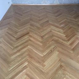 Sebud - Ułożona parkietowa podłoga w jodełkę, widoczne ślady po szpachlowaniu ścian przy podłodze.