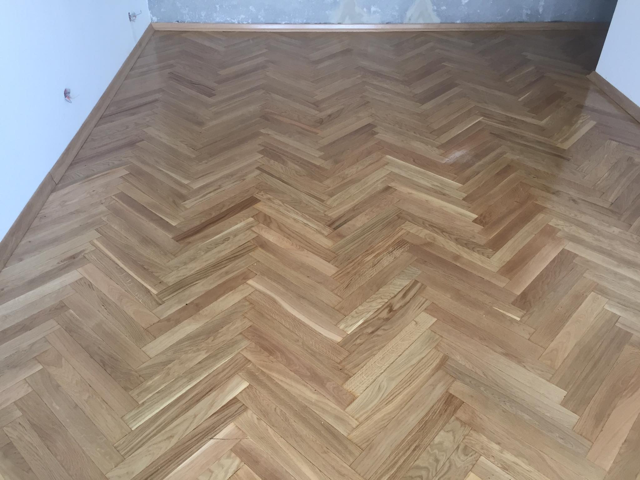 Ułożona parkietowa podłoga w jodełkę, widoczne ślady po szpachlowaniu ścian przy podłodze.