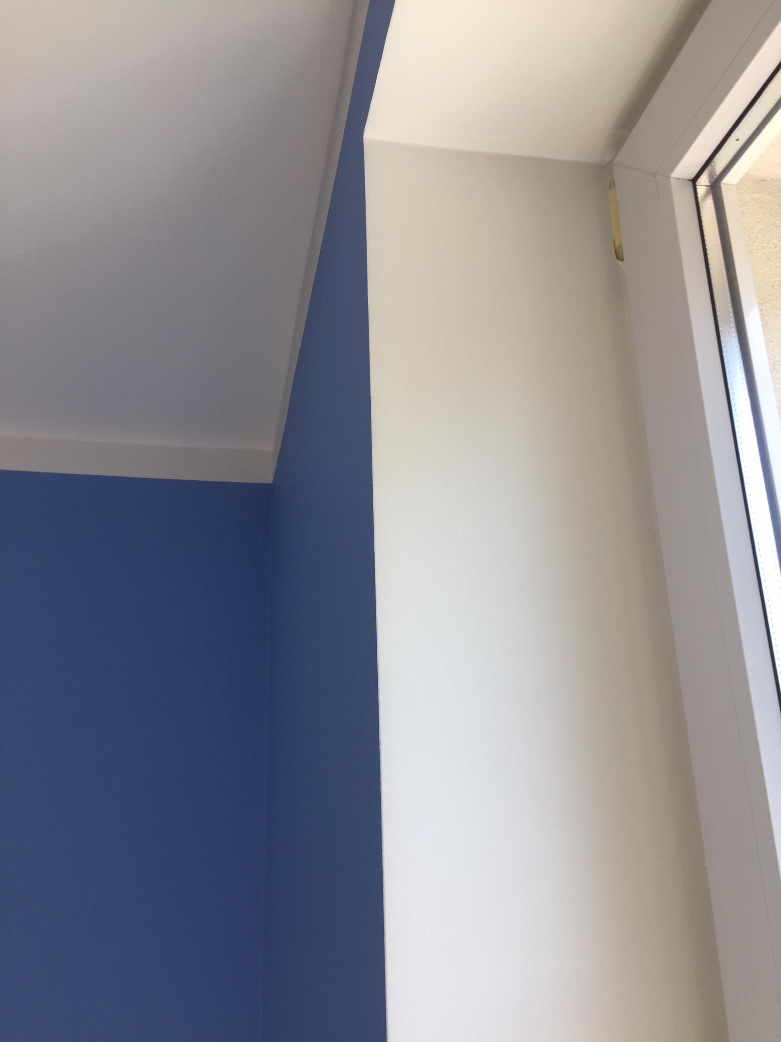 Fragment wnętrza po malowaniu: intensywny niebieski kolor ściany kontrastuje z białą ścianą przy oknie, widoczne precyzyjne wykończenie narożników i listew przysufitowych.