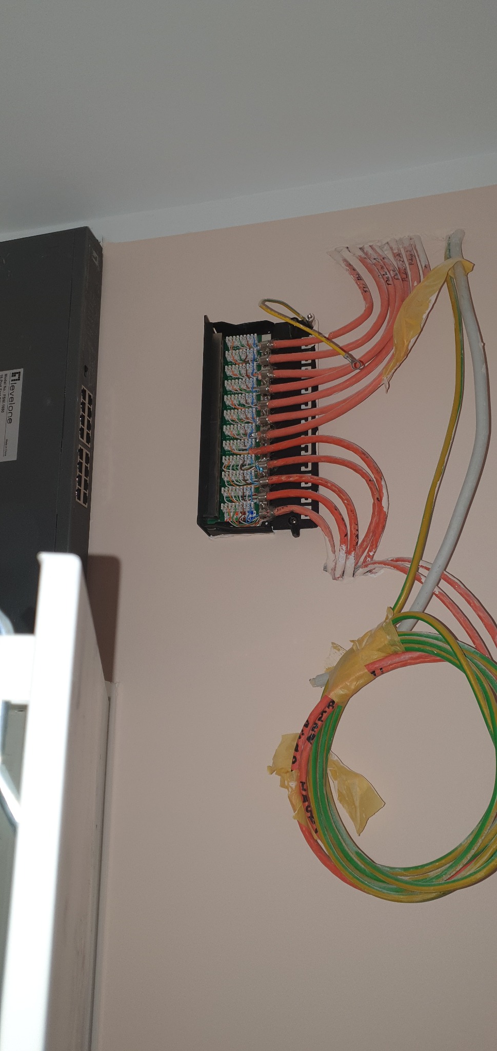 Panel krosowniczy z podłączonymi kablami sieciowymi, widoczny switch sieciowy po lewej stronie, kable tymczasowo zabezpieczone taśmą malarską.