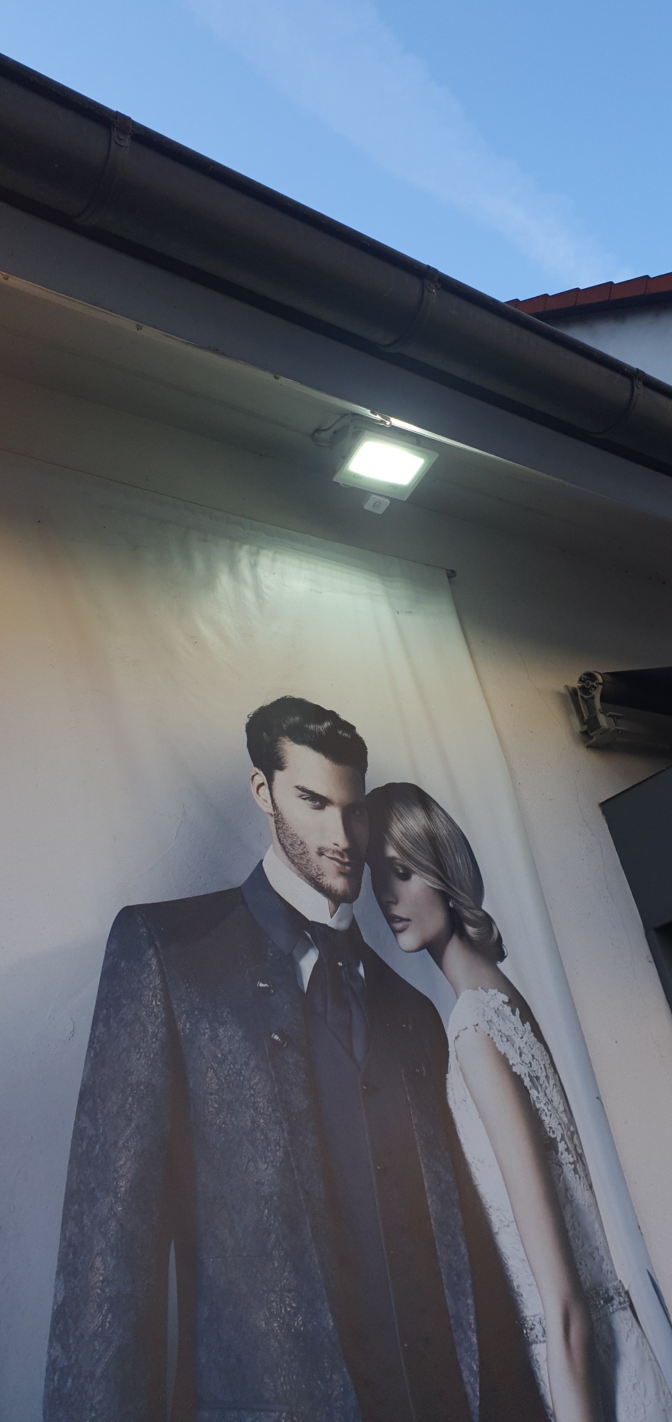 Reklama salonu ślubnego: para młoda w eleganckich strojach na plakacie pod oświetleniem zewnętrznym.