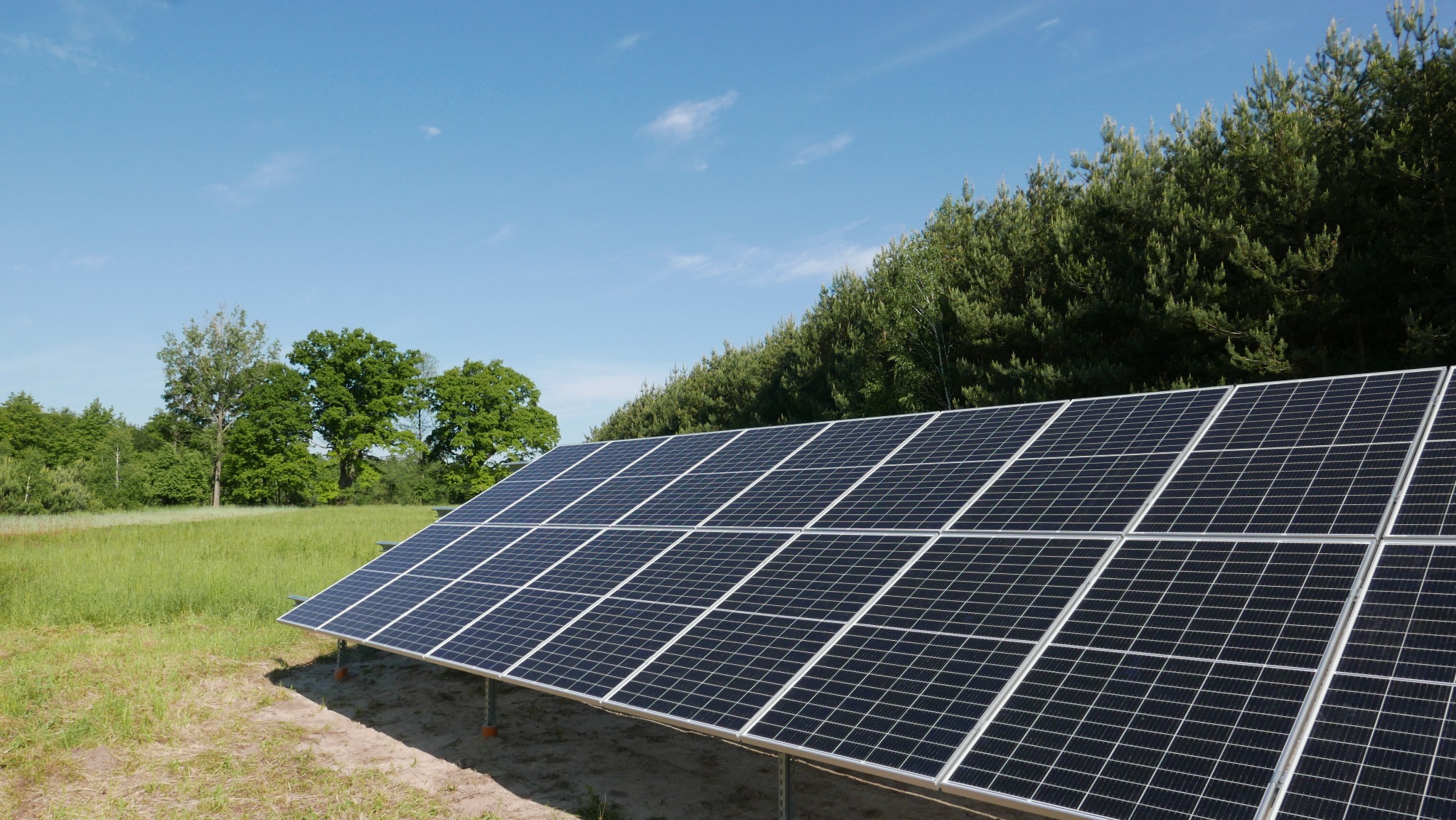Panel słoneczny na tle zieleni i błękitnego nieba. Widoczne moduły fotowoltaiczne zamontowane na konstrukcji wsporczej. Energia odnawialna w otoczeniu natury.