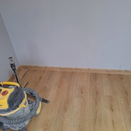 Usługi Budowlane - Fragment pokoju z nowo ułożoną podłogą z paneli, widoczny odkurzacz przemysłowy Stanley i listwy przypodłogowe z MDF w kolorze drewna.