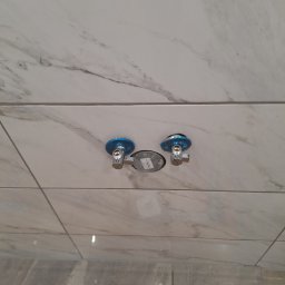 Usługi Budowlane - Białe płytki imitujące marmur z zamontowanymi zaworami kątowymi z niebieskimi osłonami, widoczne narzędzia i akcesoria montażowe na podłodze.