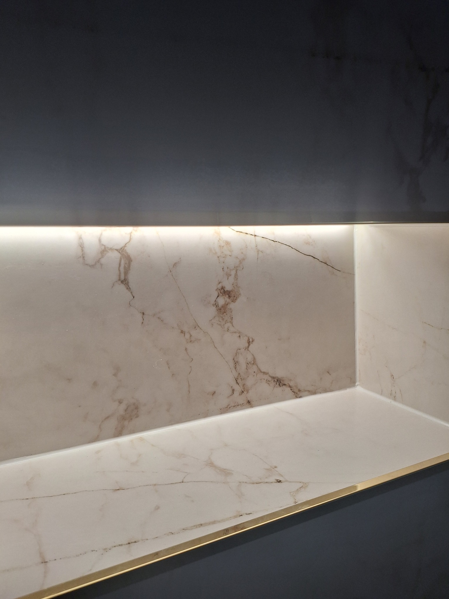 Wykończona wnęka z marmurową płytką, podświetlona listwą LED, z eleganckim złotym wykończeniem krawędzi. Ciemne tło podkreśla detale i luksusowy charakter.