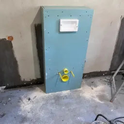 Stelaż podtynkowy do WC zabudowany płytą gipsowo-kartonową z widocznymi żółtymi rurami przyłączeniowymi, w trakcie montażu w surowym pomieszczeniu z widocznymi śladami prac remontowych na ścianach...